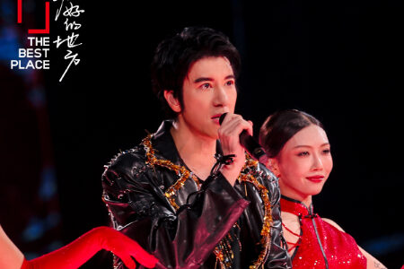 Leehom performing with a female co-performer in traditional red dress, both holding microphones on stage