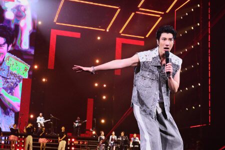 Leehom in a sleeveless denim vest performing with geometric orange neon lighting patterns in the background
