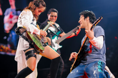Leehom playing electric guitar alongside a female guitarist in an energetic concert performance